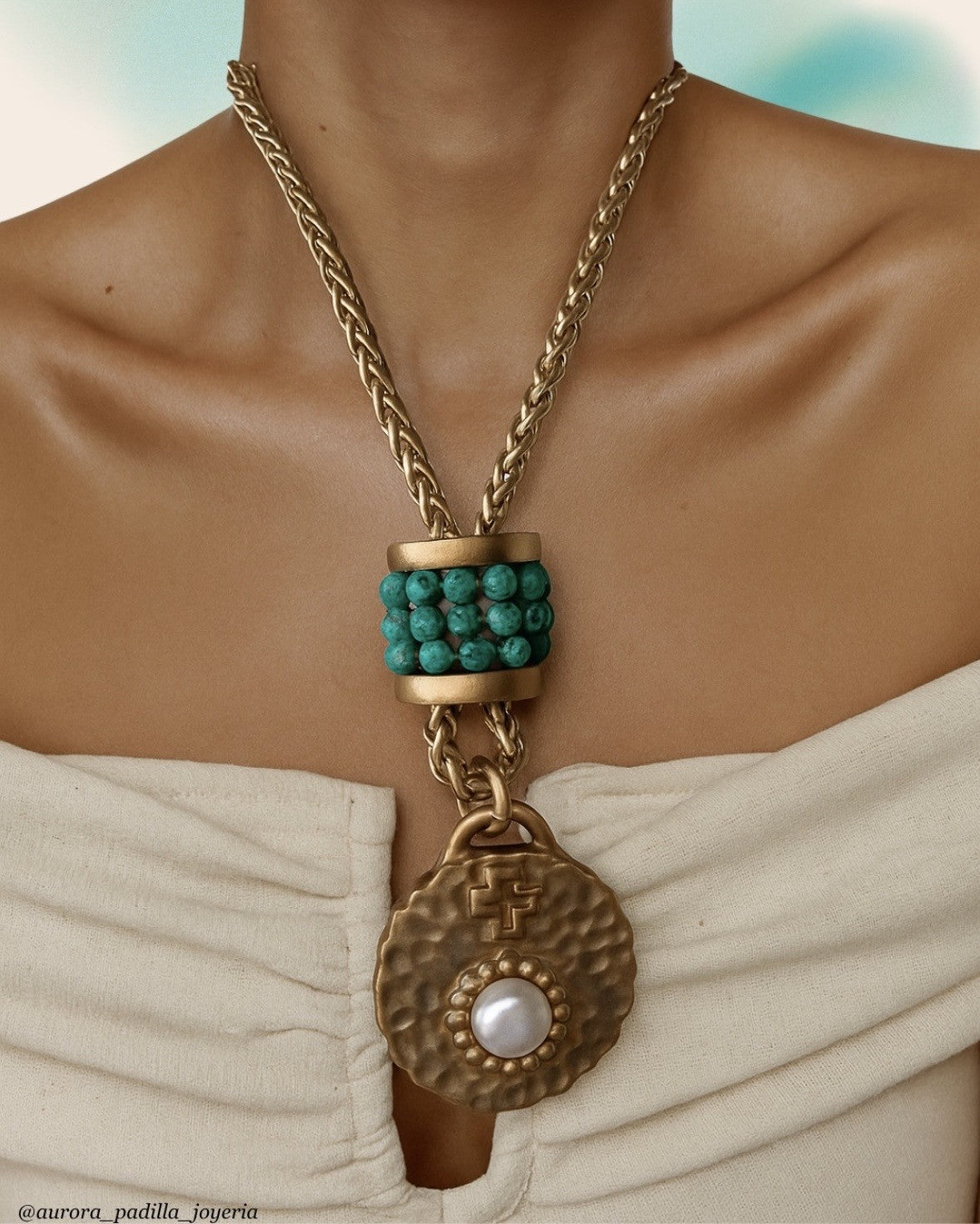Necklace with turquoise beads and gold chain on a person wearing a white garment.